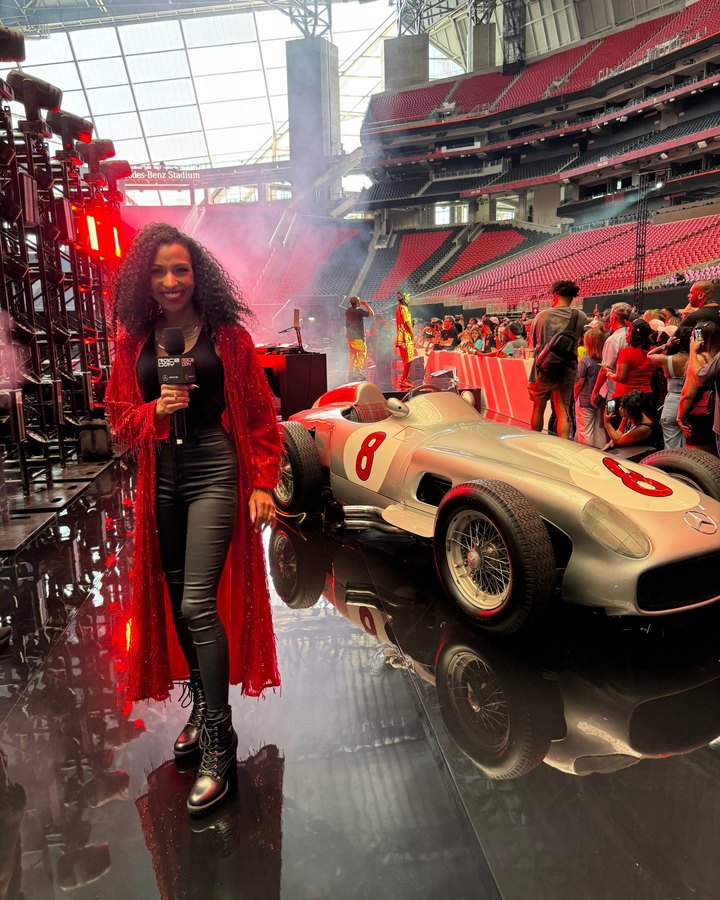 Chelsea with a Race Day mic beside a classic silver Mercedes race car inside Mercedes-Benz Stadium