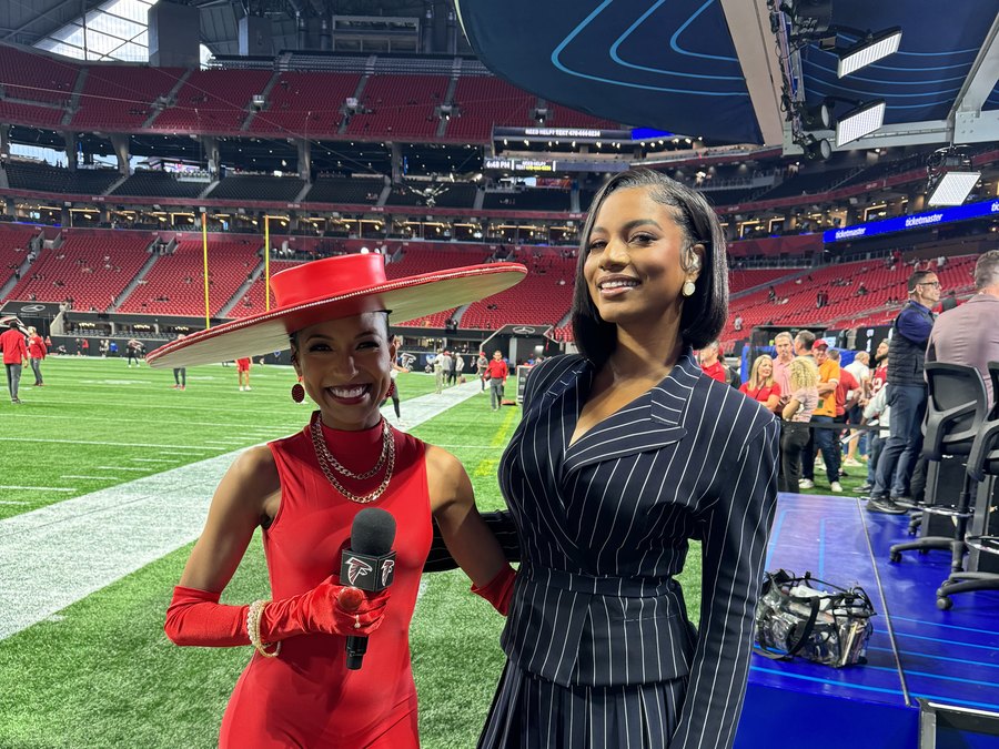 Chelsea in a red jumpsuit and wide-brim hat with a Falcons mic, on the sideline at Mercedes-Benz Stadium