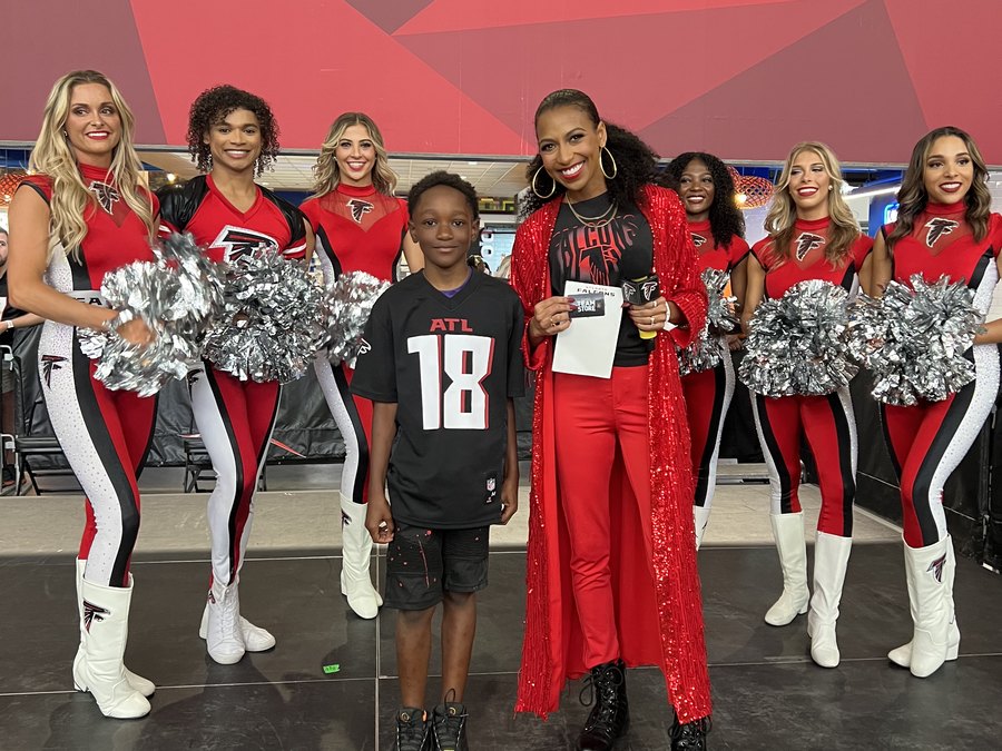 Chelsea running a fan game on the field with a young fan and the Falcons cheerleaders